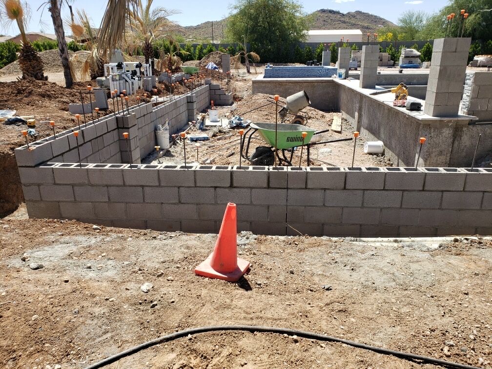 Backyard with capped rebar, finished perimeter block wall, and traffic cone in foreground