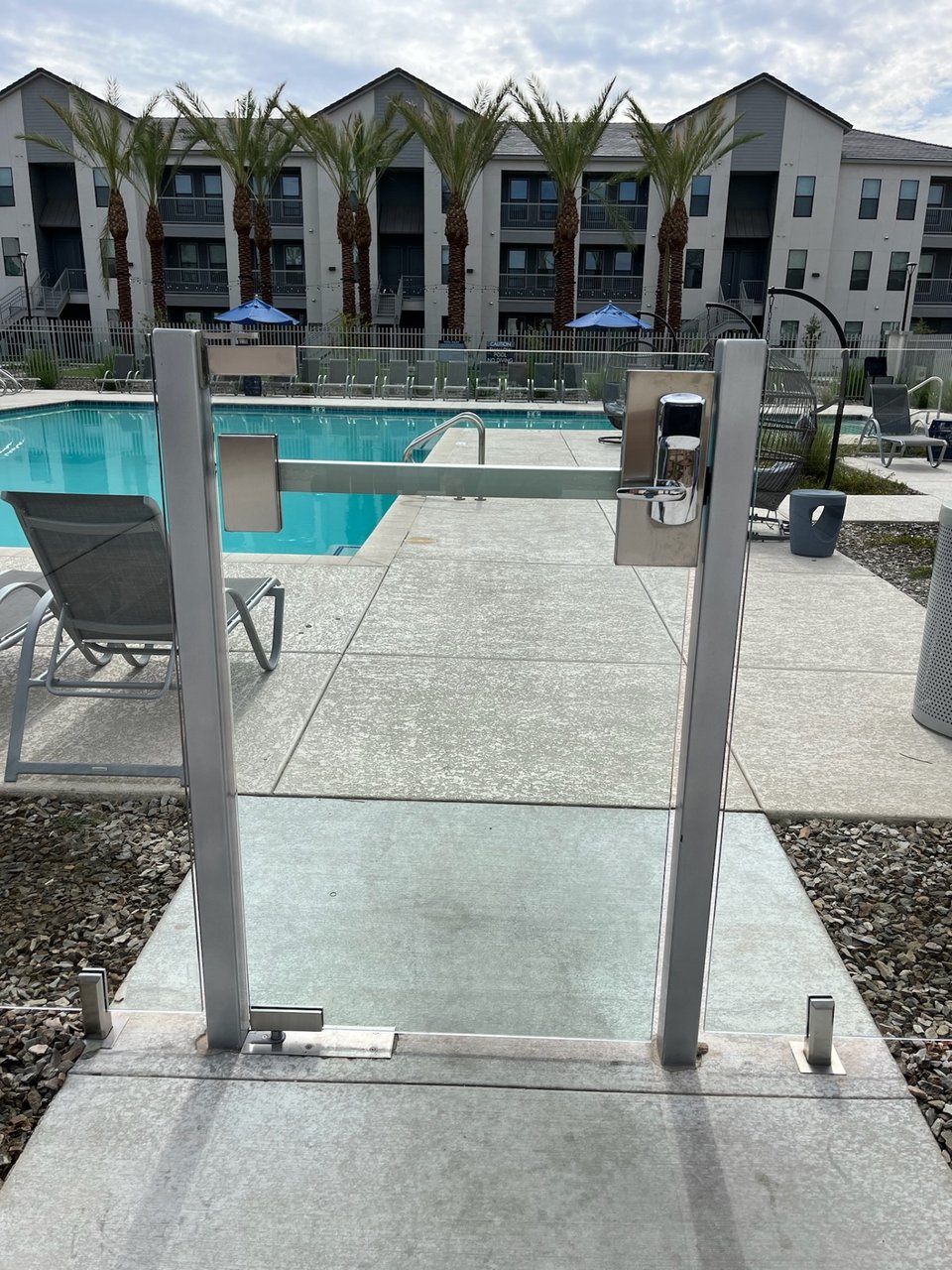 Close-up of a glass gate assembly with access-control hardware at an apartment pool area.