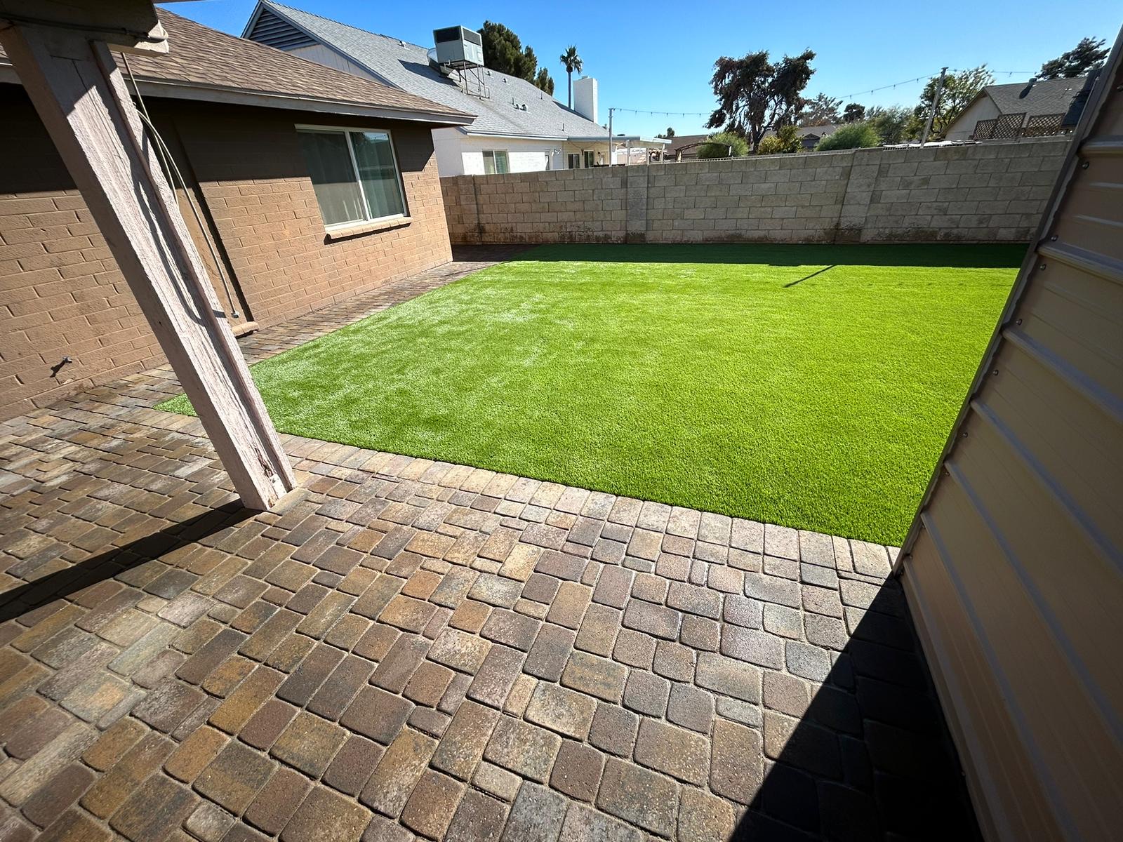 Tumbled paver patio meeting a fresh turf lawn under a covered back porch.