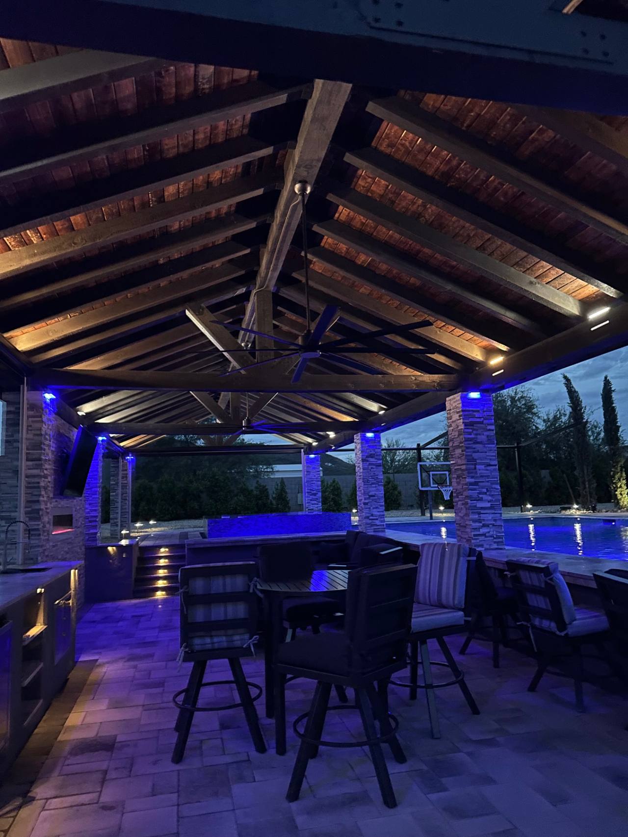 Night interior of a heavy timber ramada with lighting, fans, and exposed wood ceiling detail.