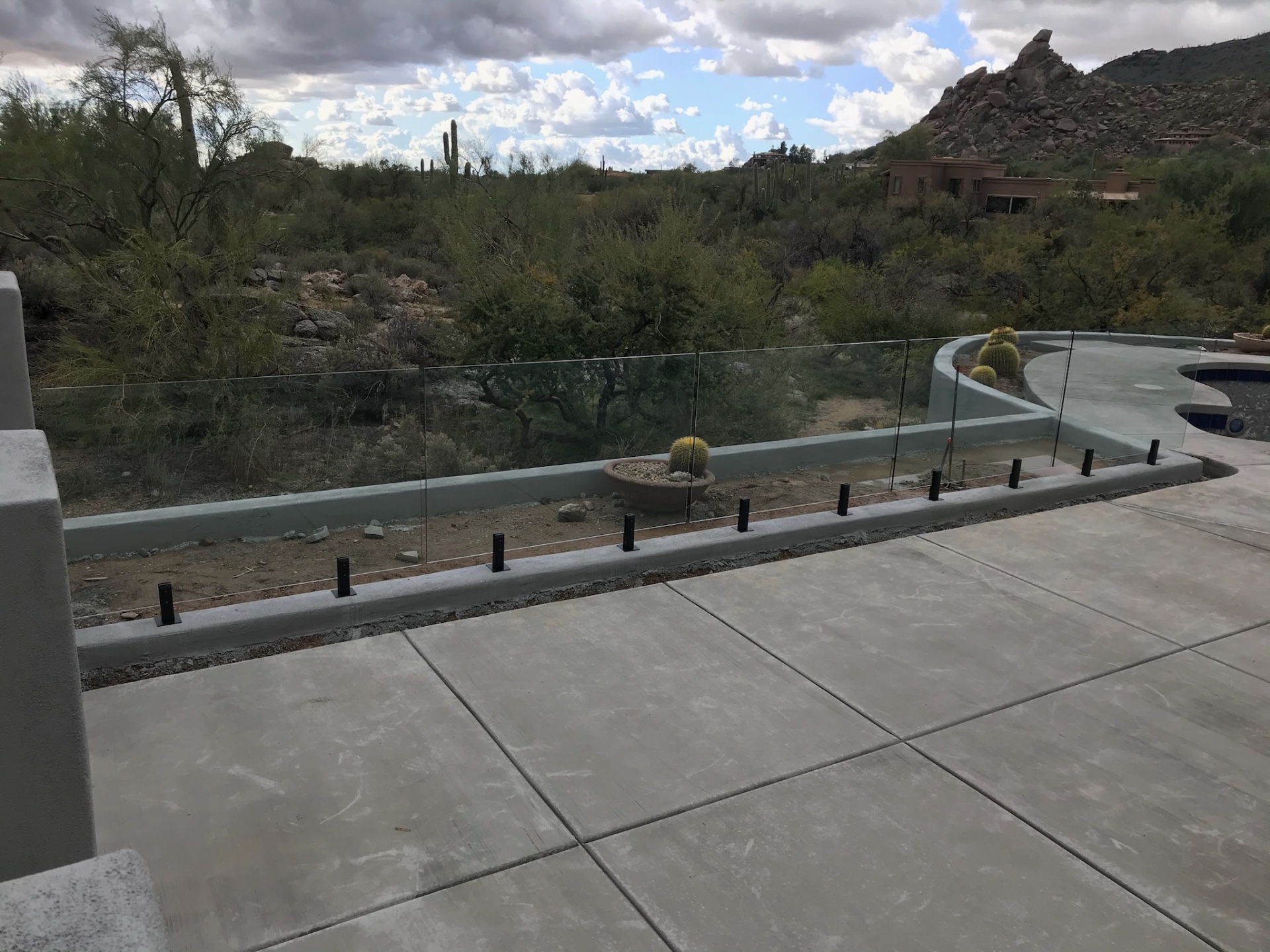 Frameless glass pool fence following a curved bond beam around a desert pool with mountain and saguaro views in the background.