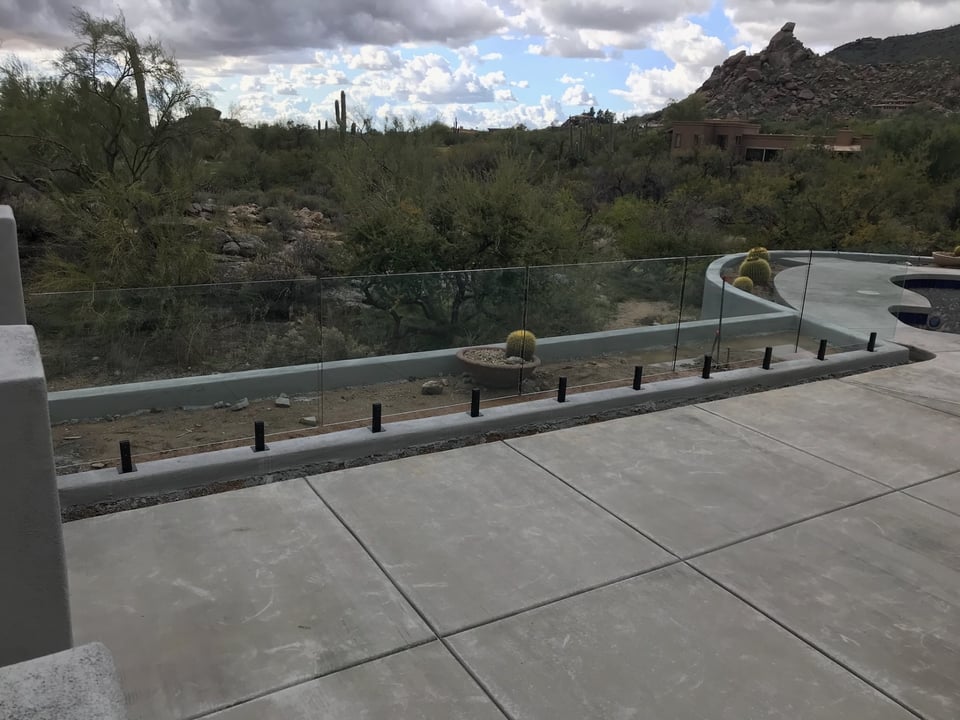 Frameless glass fence panels following a curved concrete curb around a desert pool, with mountain and saguaro views beyond.