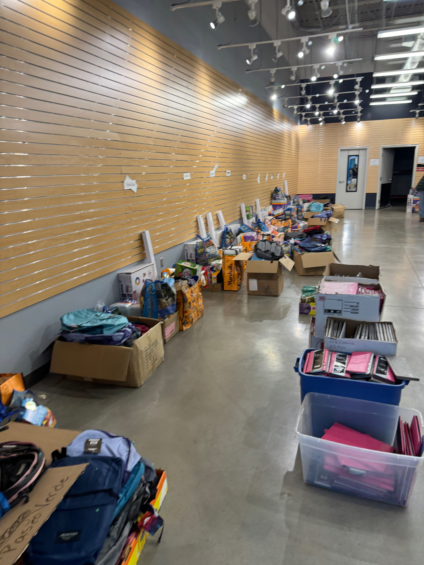 Backpacks and supply boxes staged by neighborhood with handwritten signs like Paseo Verde before distribution