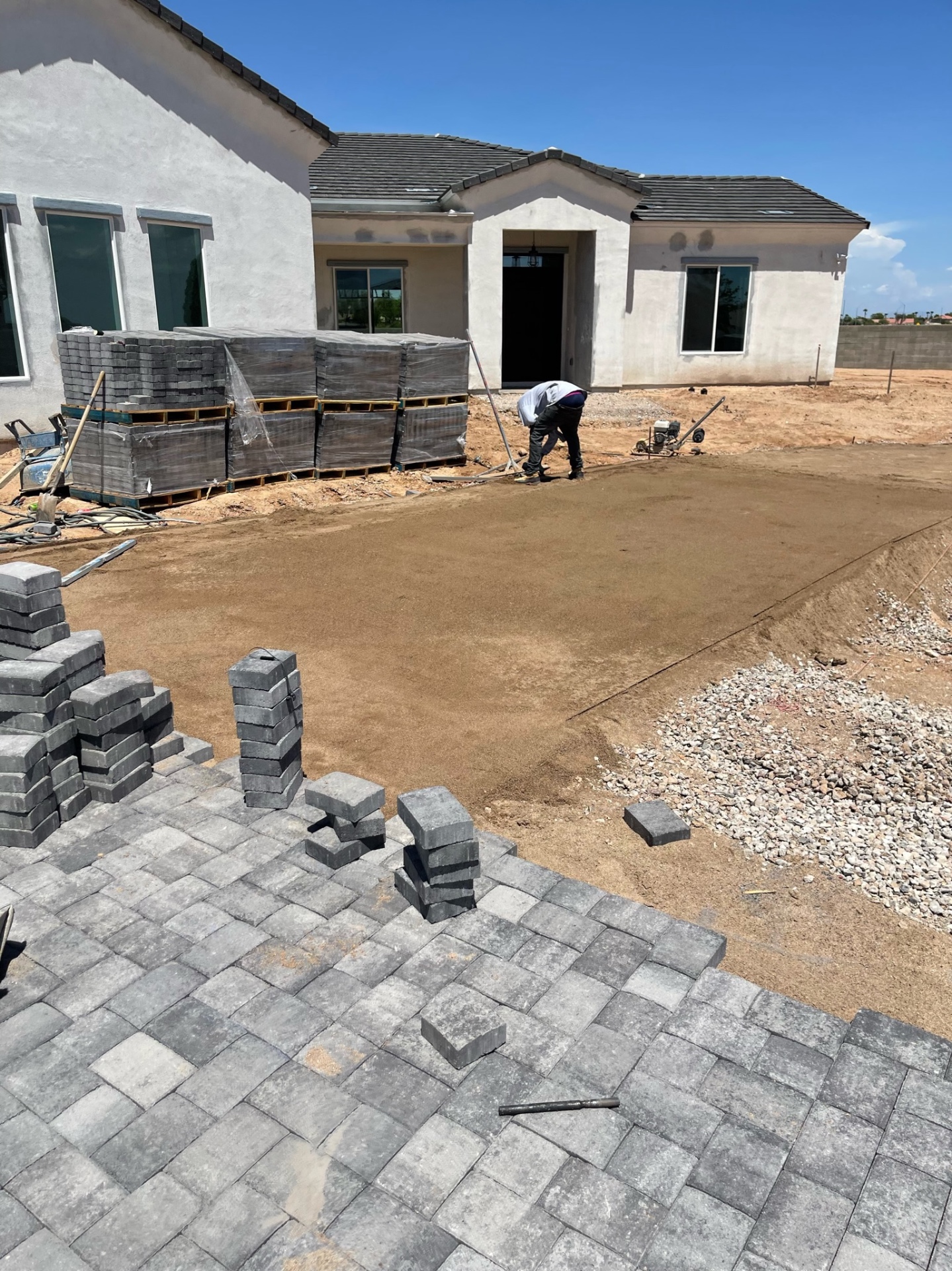 Waddell (Surprise-area) AE Outdoor Living crew screeding a 1-inch sand bed over compacted ABC base ahead of paver install — canonical AE base spec