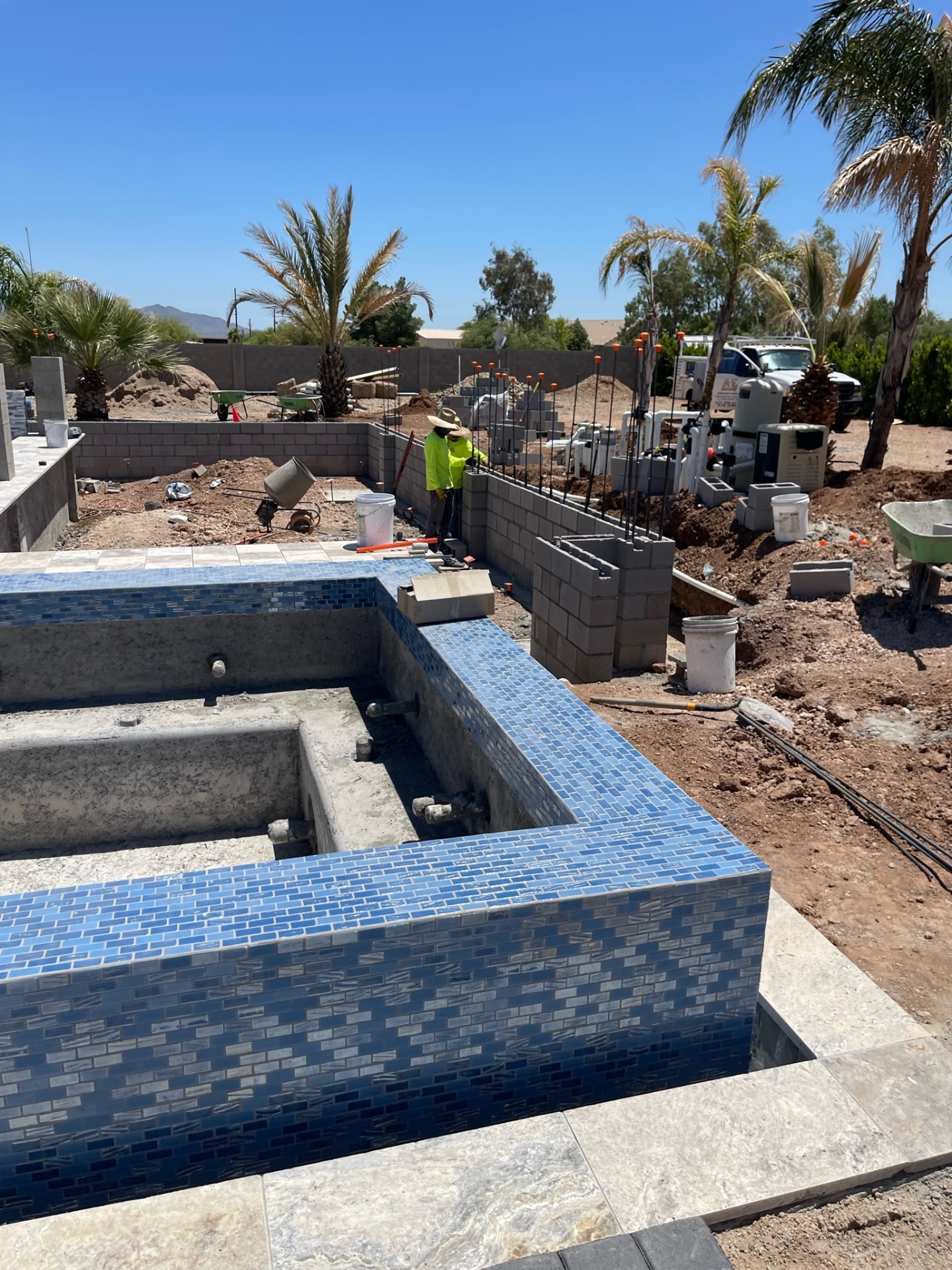 Pool shell and raised tiled spa with a block wall under construction and AE truck visible near the far edge of the jobsite