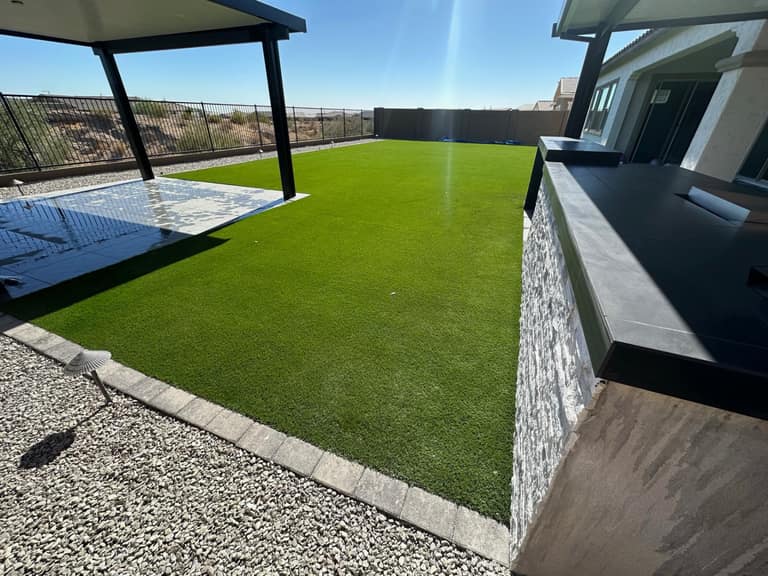 Turf lawn framed by paver soldier course, view fence, and porcelain-tile seat wall with stacked-stone base.