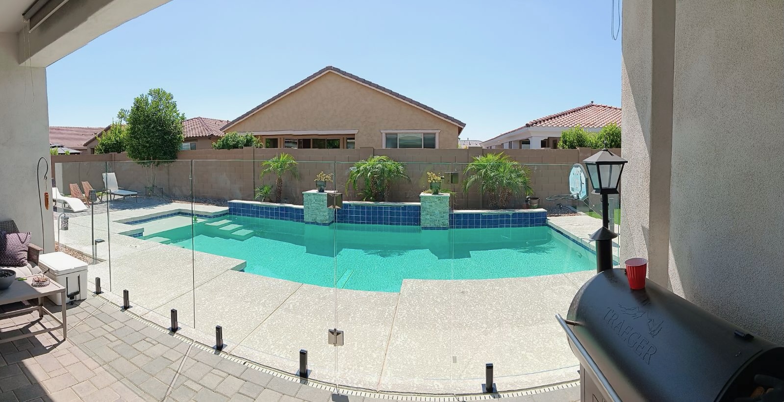 Thorn residence, Mesa AZ — wide view of the freeform pool with dark blue waterline tile, twin stacked-stone raised planter columns with palms, and frameless glass pool fence.