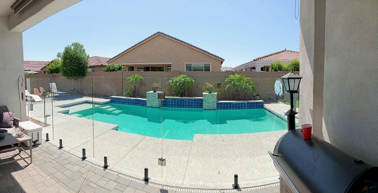 Thorn residence Mesa AZ wide view of freeform pool with dark blue waterline tile, twin stacked-stone raised planter columns with palms, cool-deck patio, and frameless glass pool fence