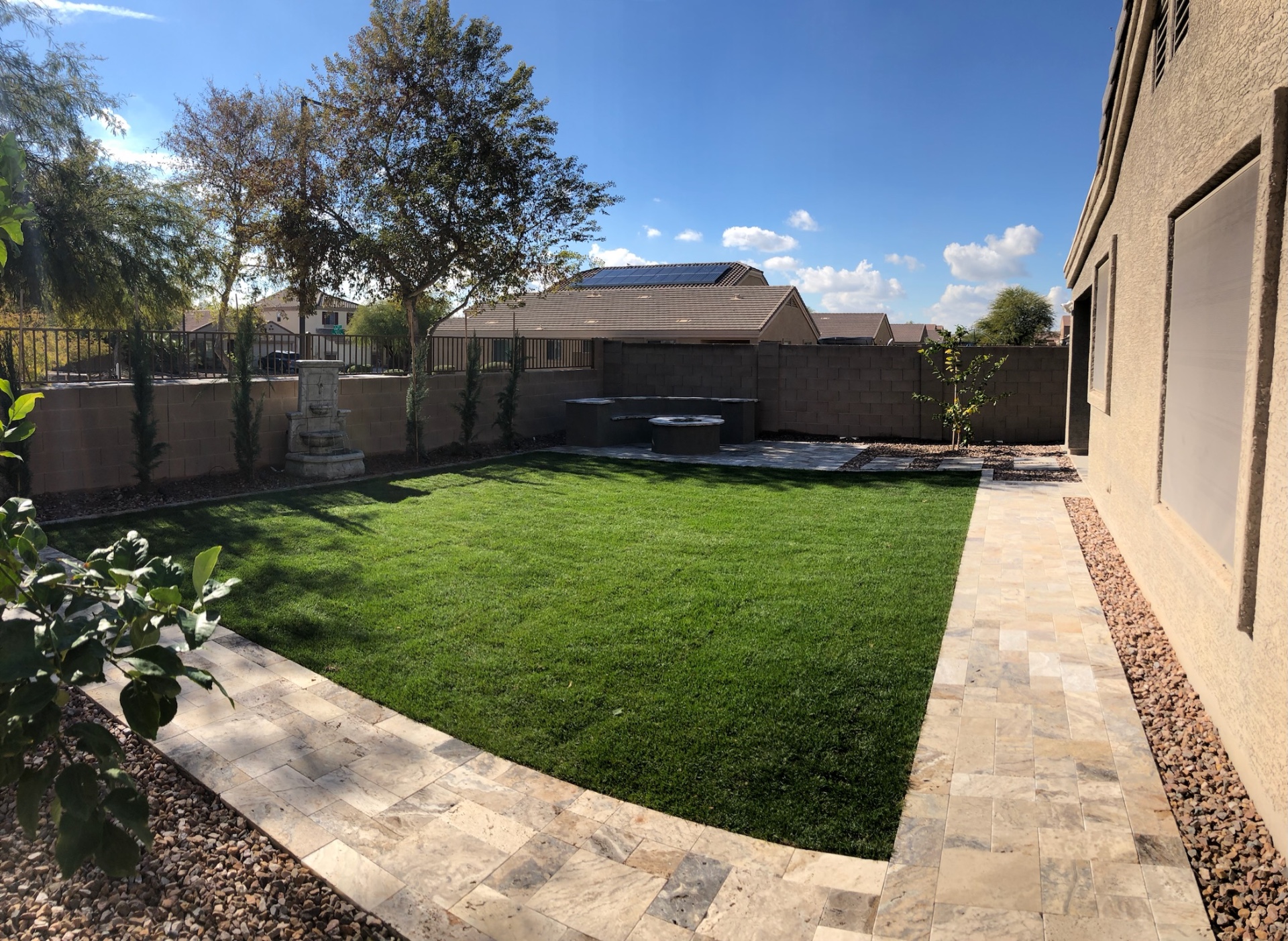 Verrado backyard in Buckeye with artificial turf lawn, travertine paver ribbon, and fire-pit patio by AE Outdoor Living