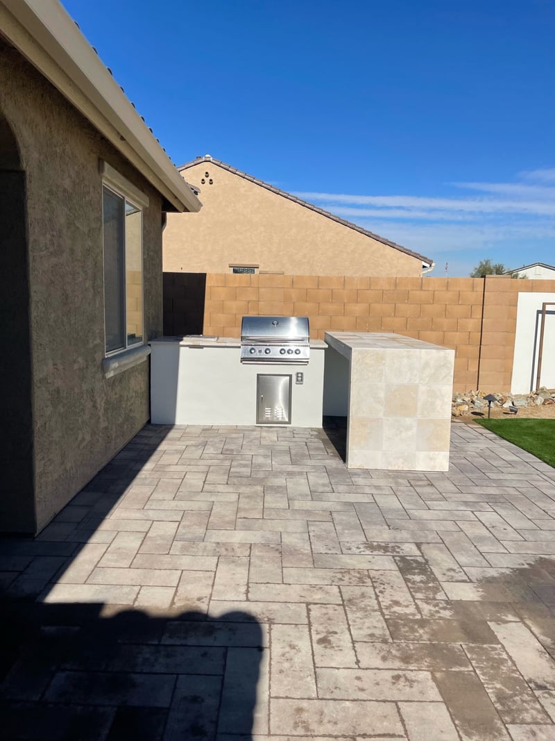 Goodyear paver patio with built-in stucco BBQ island, travertine-tile bar counter and stainless grill by AE Outdoor Living