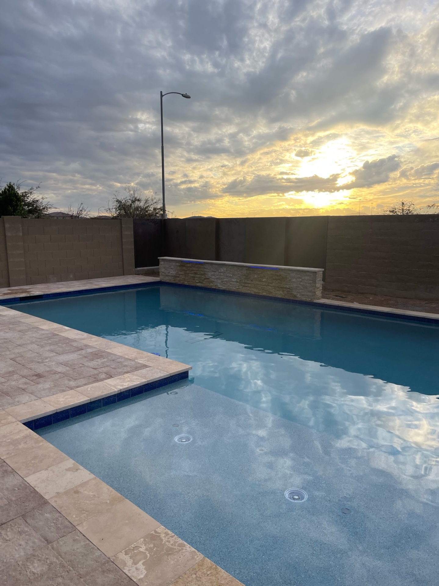 Peoria custom pool with tanning ledge, stacked-stone raised water wall with LED wash and travertine paver deck at dusk