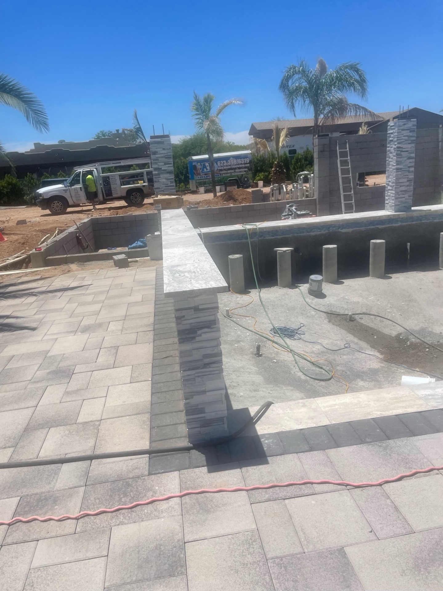 Stacked-stone column with travertine cap and paver deck, AE Outdoor Living truck visible in background