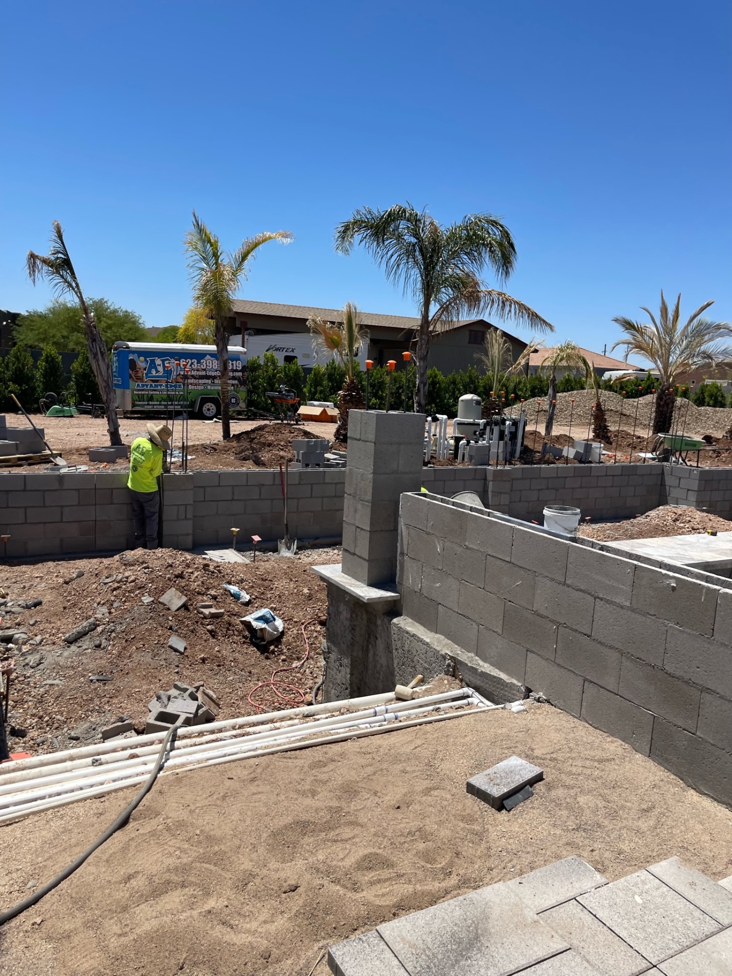 AE Advant-Edge trailer on jobsite with crew member laying block wall and palm trees behind