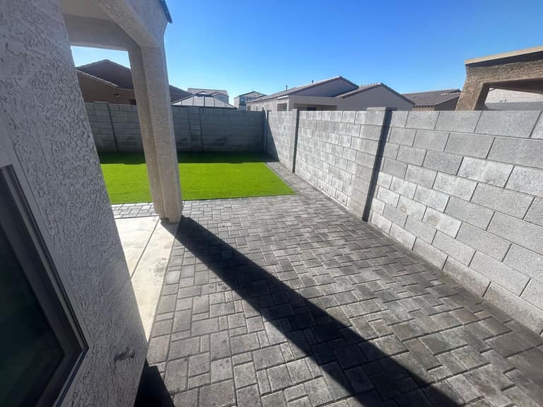 Charcoal paver side-yard patio and rear pad meeting a bright artificial turf rectangle in a compact backyard.