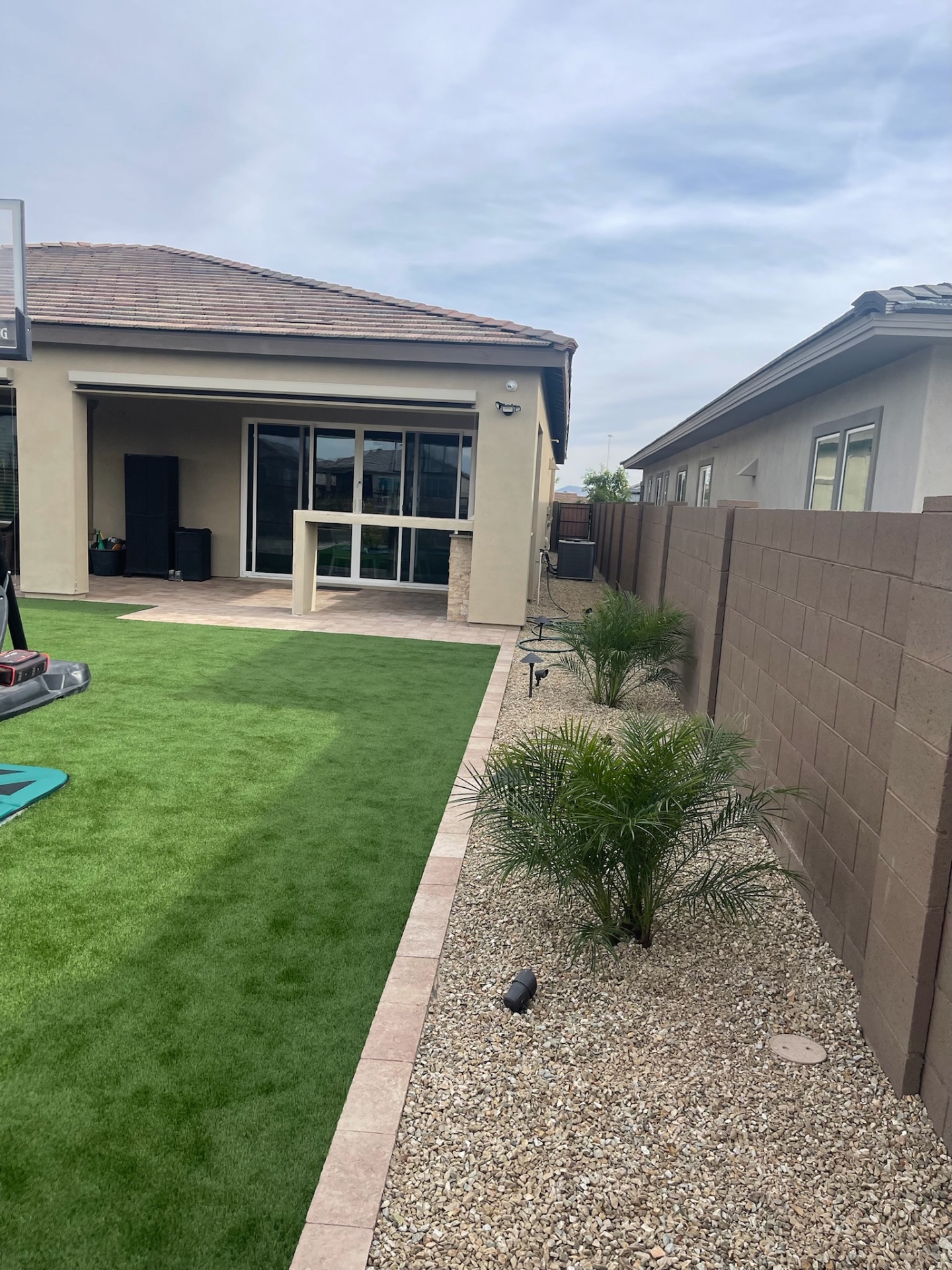 Peoria backyard artificial turf lawn with travertine paver border and desert palm plantings against block privacy wall