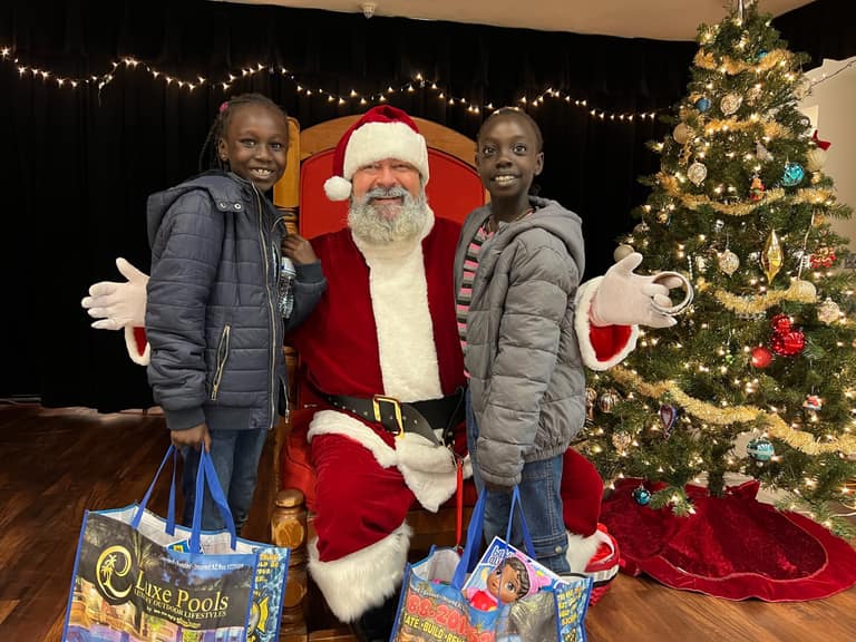 Two sisters with Santa holding AE Outdoor Living Luxe Pools branded gift bags at Shop With a Cop