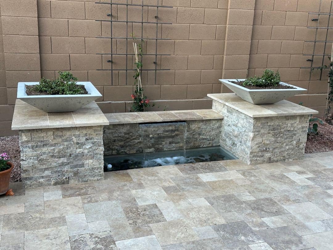 Stacked-stone spillway water feature with travertine caps in a Peoria backyard