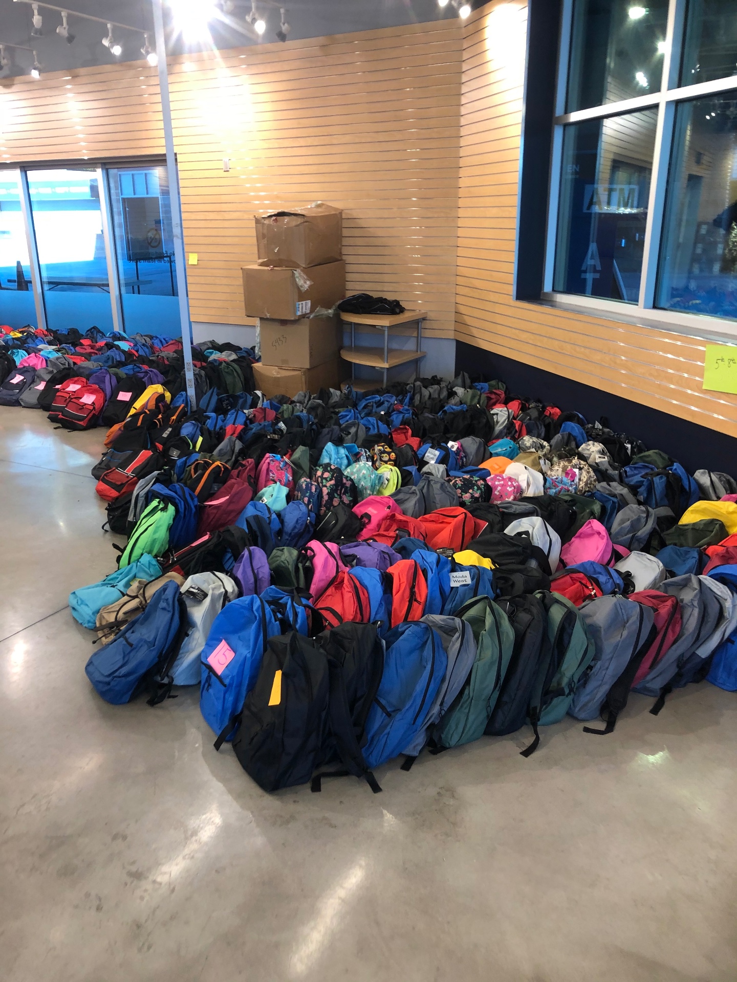 Hundreds of filled backpacks staged by grade level along the wall at the sorting facility