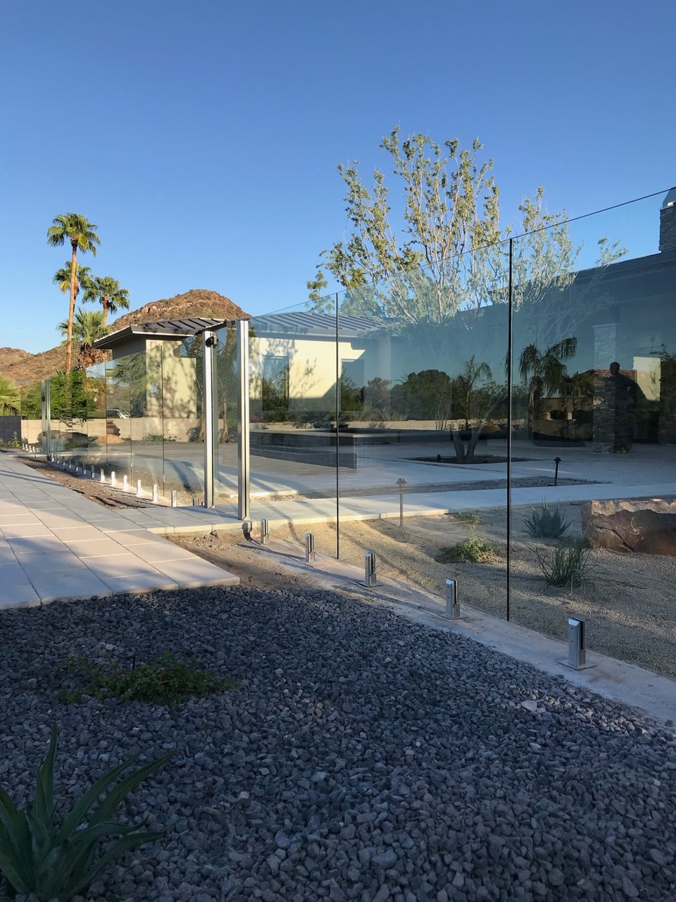 Open sightlines through glass fence panels to desert hills and palm trees beyond a pool deck.