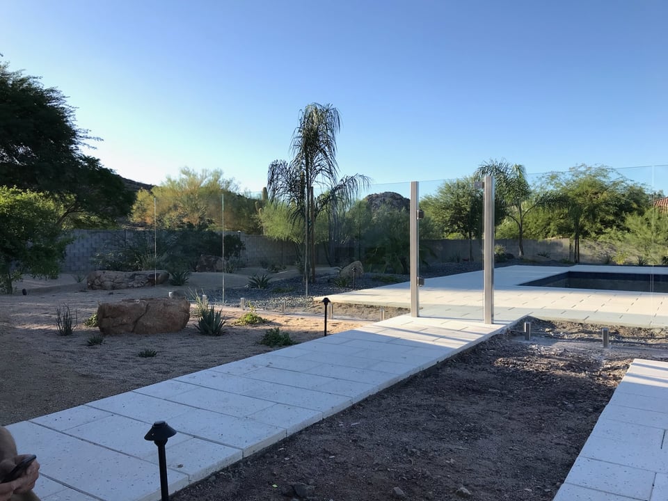 Wide approach pathway leading toward a frameless glass gate and the desert-facing pool area.