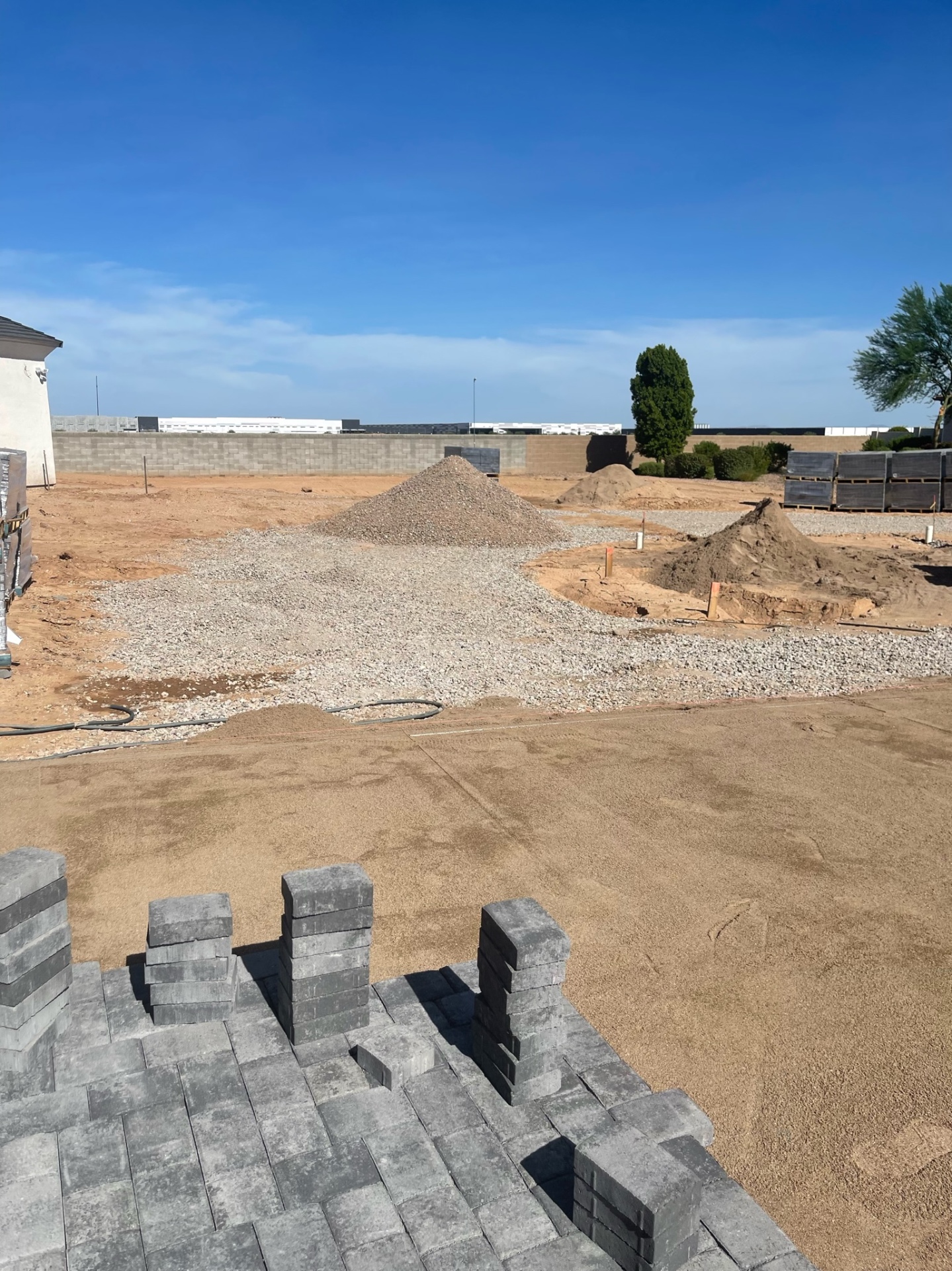 Waddell (Surprise-area) backyard paver install prep — separate piles of compacted ABC road-base and bedding sand staged next to laid charcoal paver field by AE Outdoor Living