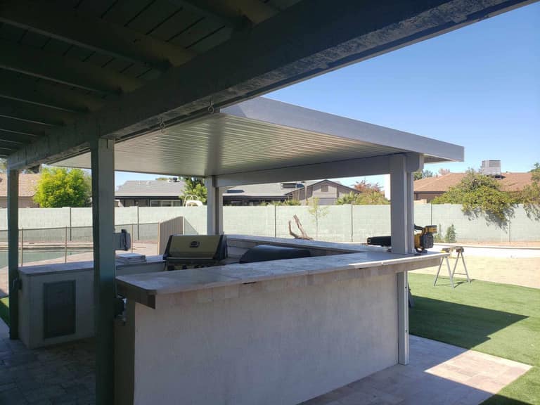Solid-roof cover over a bar and grill island — full shade, clean fascia, and fan-ready structure.