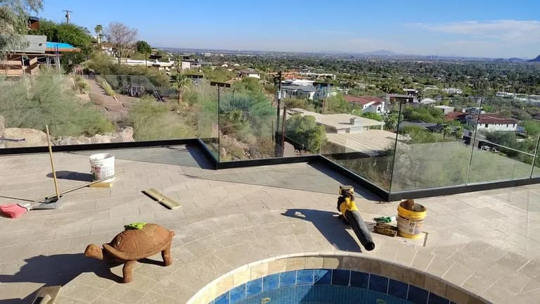 Corner of a frameless glass railing on a tiled hillside patio above the Valley.