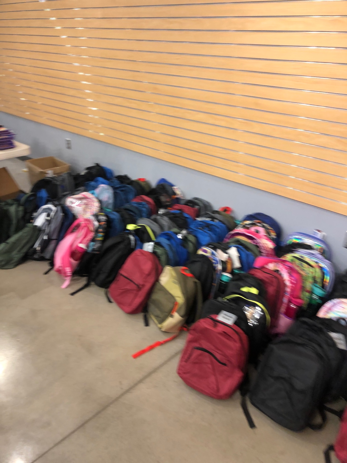 Row of completed backpacks lined against a wood-slat wall ready for distribution