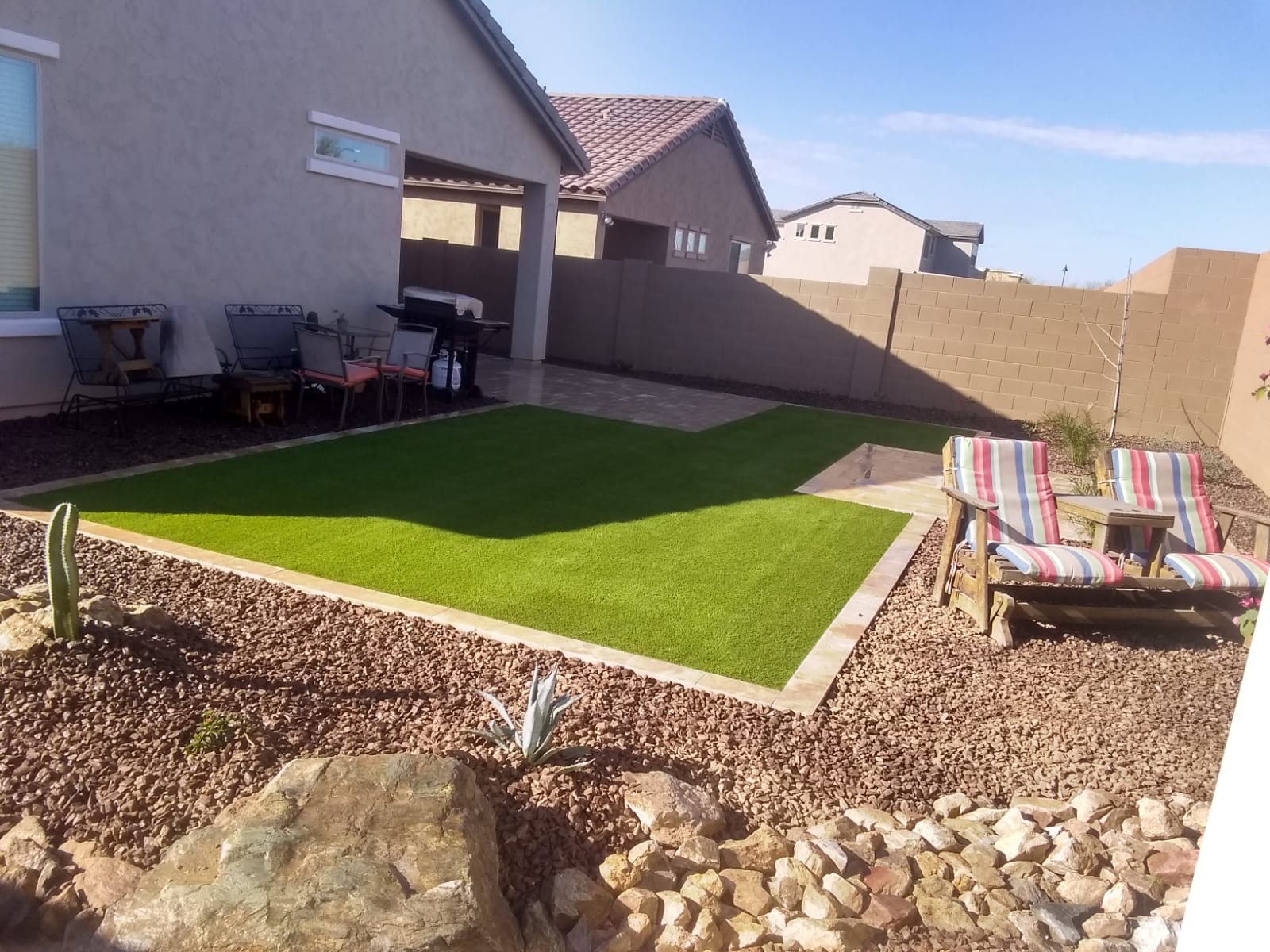 Verrado backyard turf lawn tied into a paver patio with rock border and desert plantings