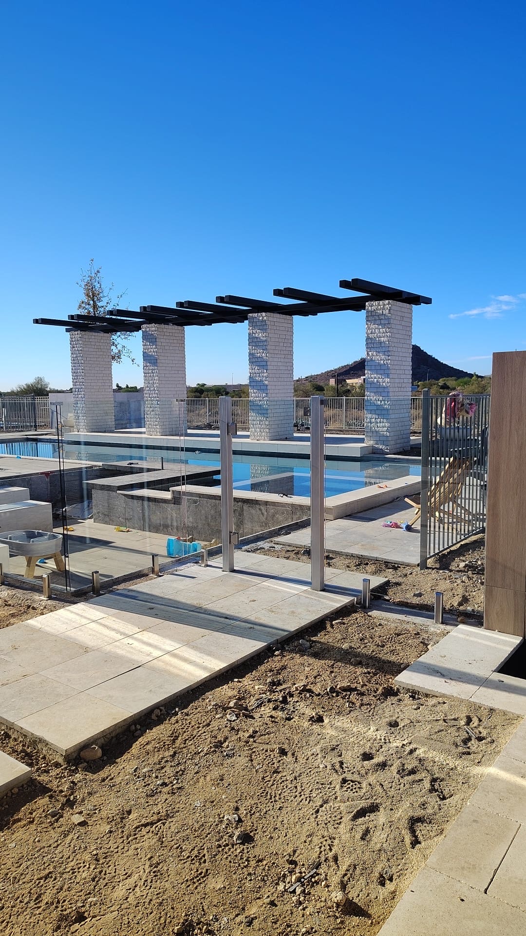 Frameless glass pool fence around a community pool with white masonry columns and steel shade beams.