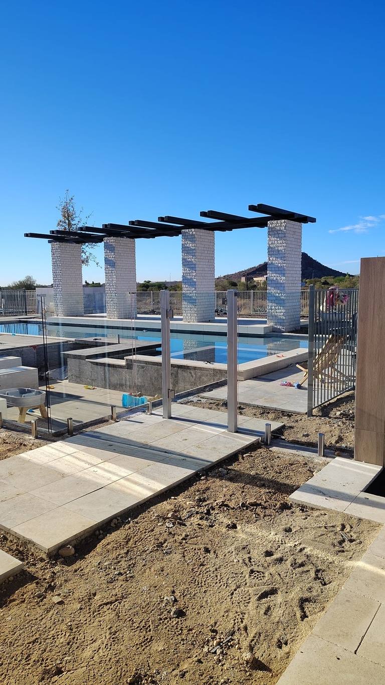 Frameless glass pool fence around a community pool with white masonry columns and steel shade beams.