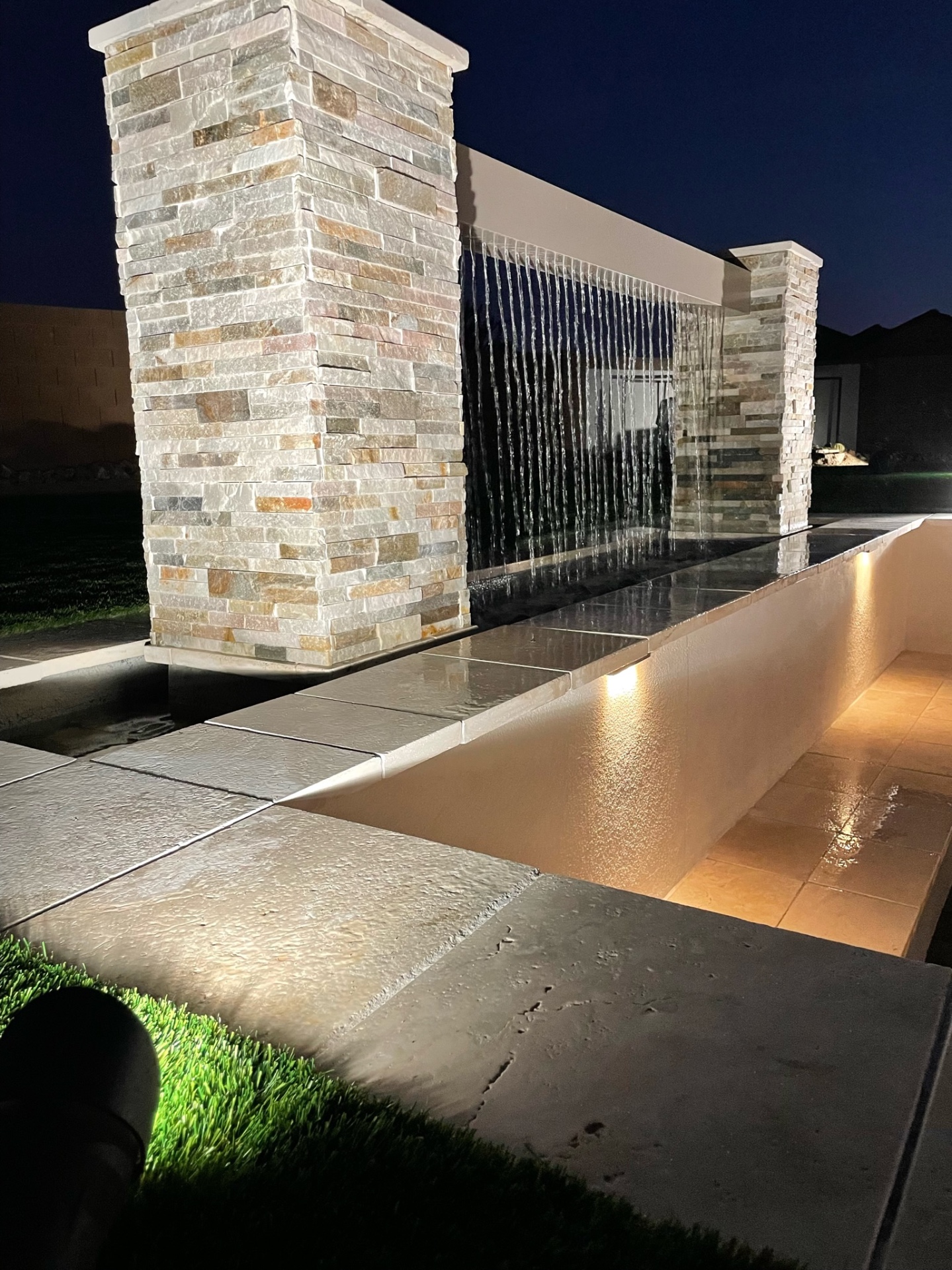 Goodyear stacked-stone waterwall detail with travertine coping, sheer-descent water sheet and paver deck
