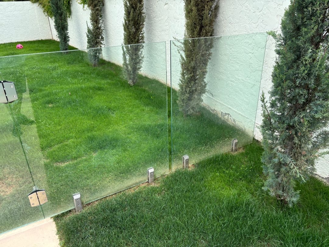 Frameless glass barrier panels with base plates visible at a narrow concrete ribbon at grade.