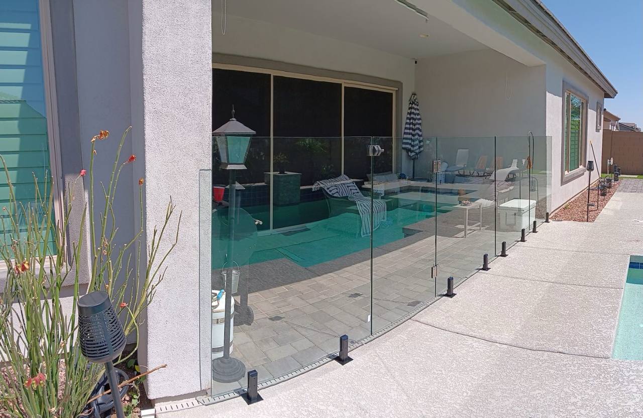 Thorn residence Mesa AZ freeform pool with sun shelf and travertine paver deck viewed from covered patio through frameless glass pool fence