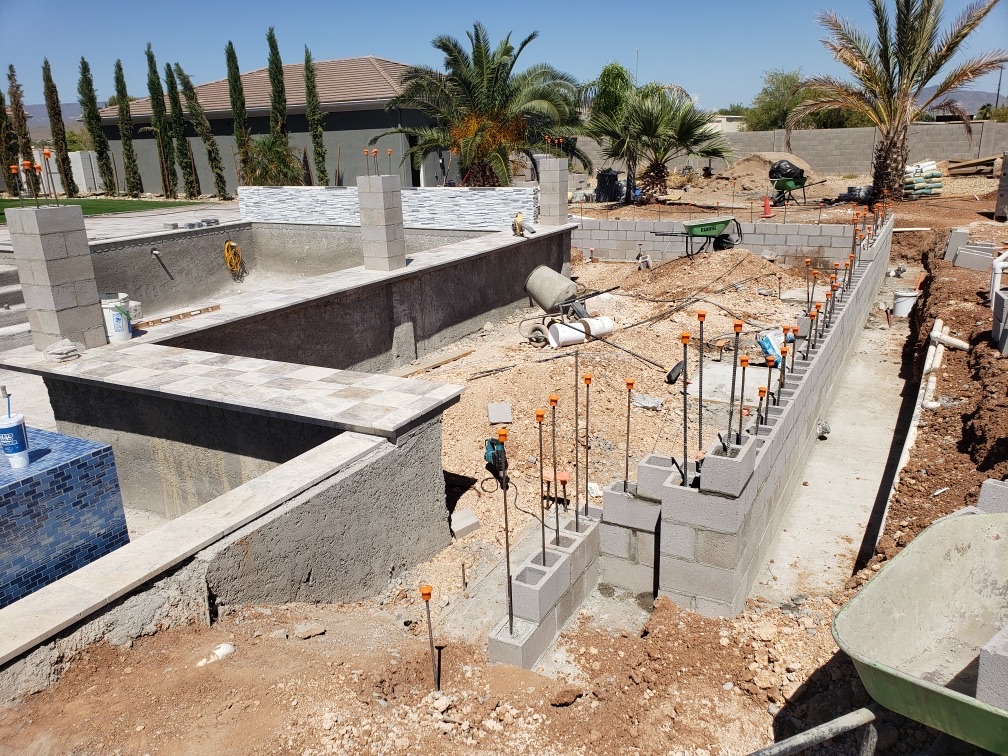 Pool with paver coping started, raised wall with stacked-stone veneer, and rebar still in adjacent wall
