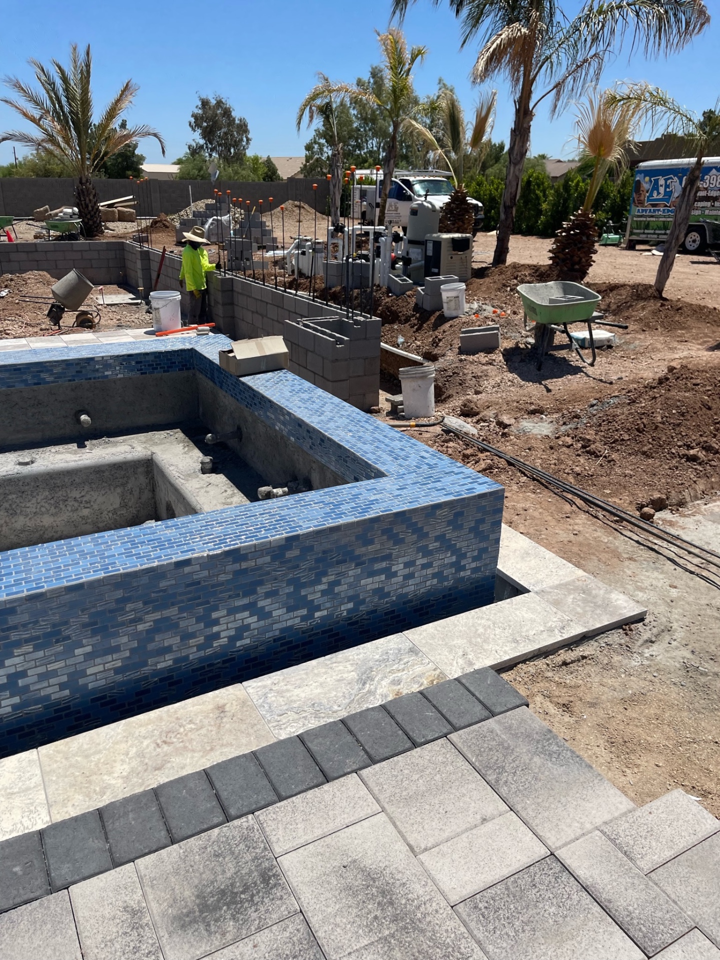 Raised tiled spa and pool shell with crew working on adjacent block wall, AE truck and trailer parked in the background
