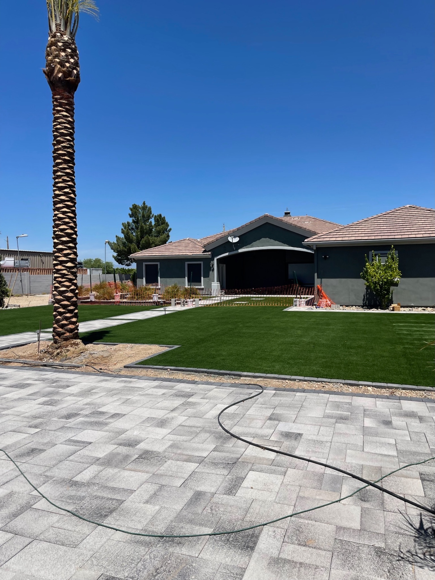 Finished front yard with mature palm, fresh artificial turf, large-format paver driveway, and walkway to a dark stucco home