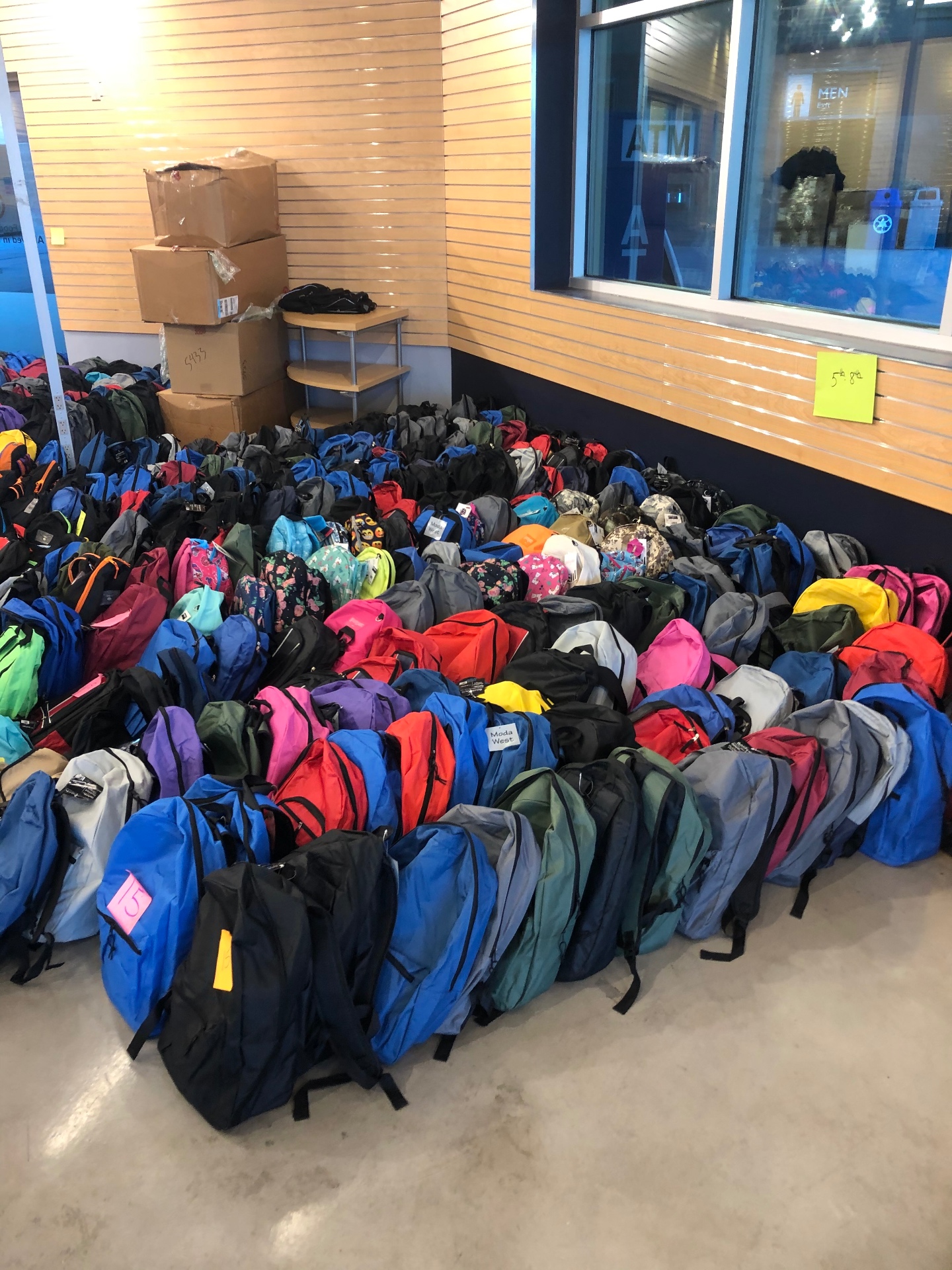 Tightly packed rows of colorful backpacks sorted near a 5th-grade signage tag