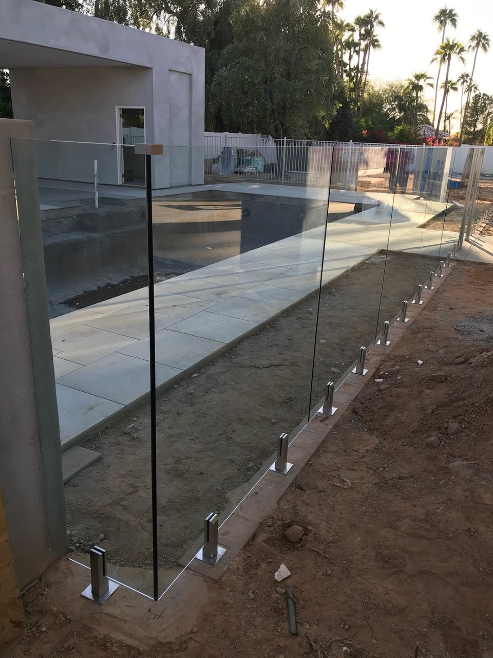 Long run of glass fence panels on spigots along a paver-finished pool deck.