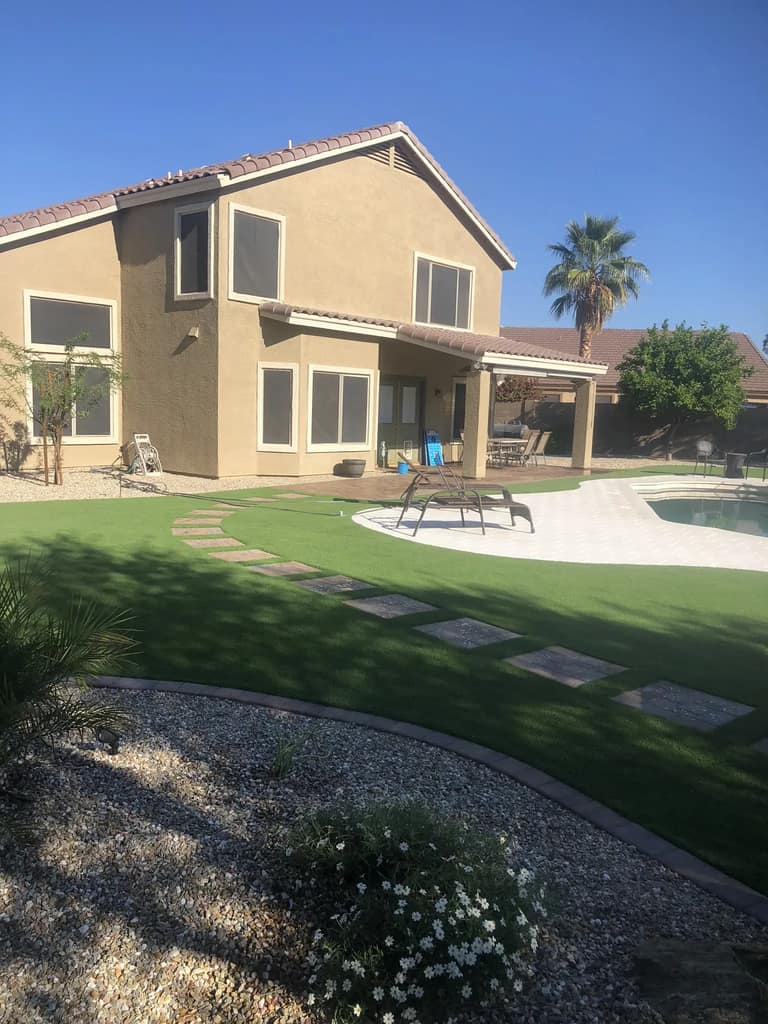 Curved paver walkway crossing artificial turf between the home, covered patio and backyard pool.