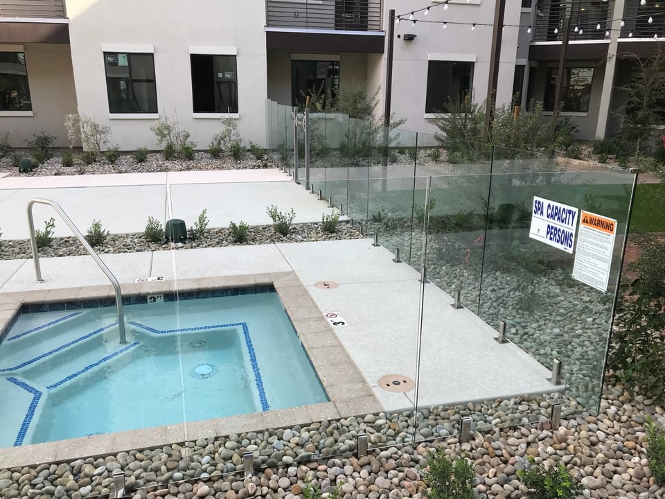 Frameless glass fence panels around a spa area, with capacity and warning signage mounted on the glass.