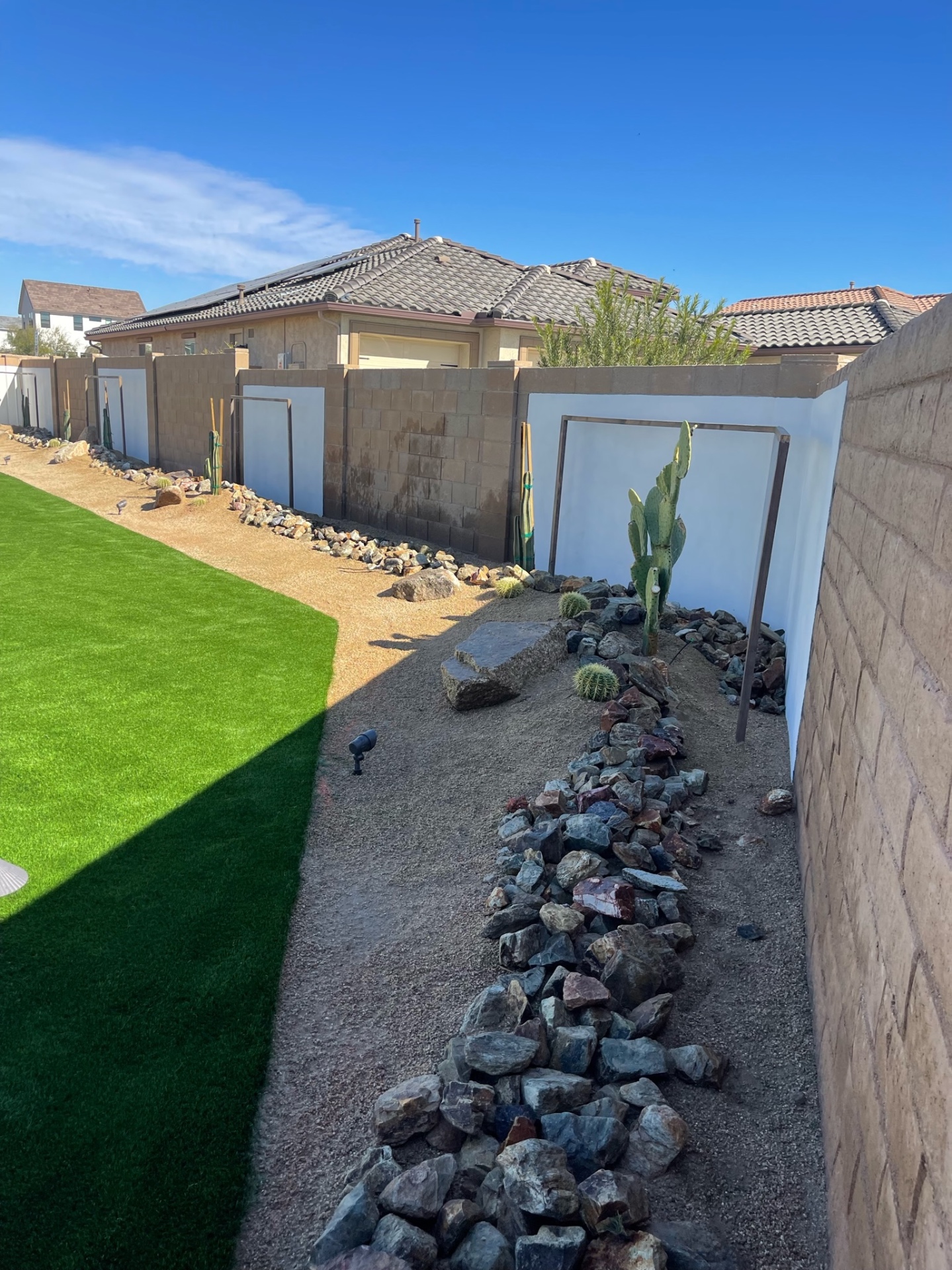 Goodyear side-yard desert-scape with cactus, boulders and rip-rap rock border meeting a fresh artificial turf runway