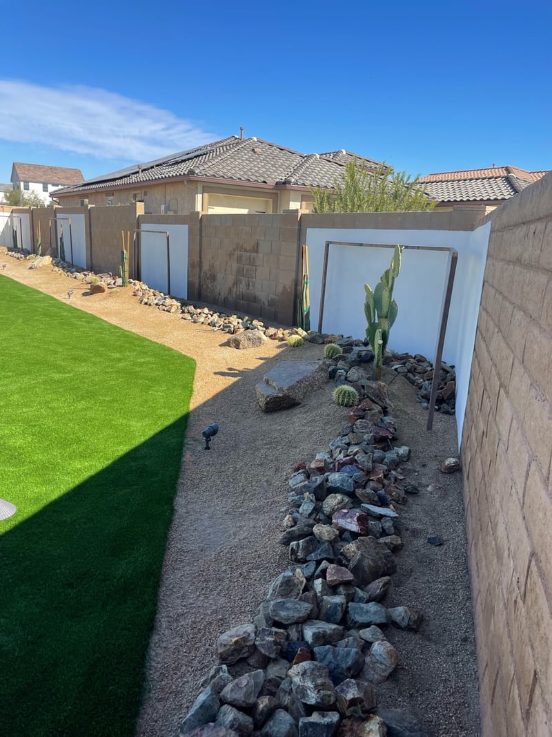 Goodyear side-yard desert-scape with cactus, boulders and rip-rap rock border meeting a fresh artificial turf runway