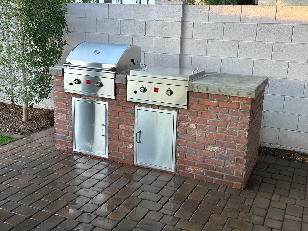 Same brick BBQ island from a working angle showing grill, side burner, and concrete counter detail.