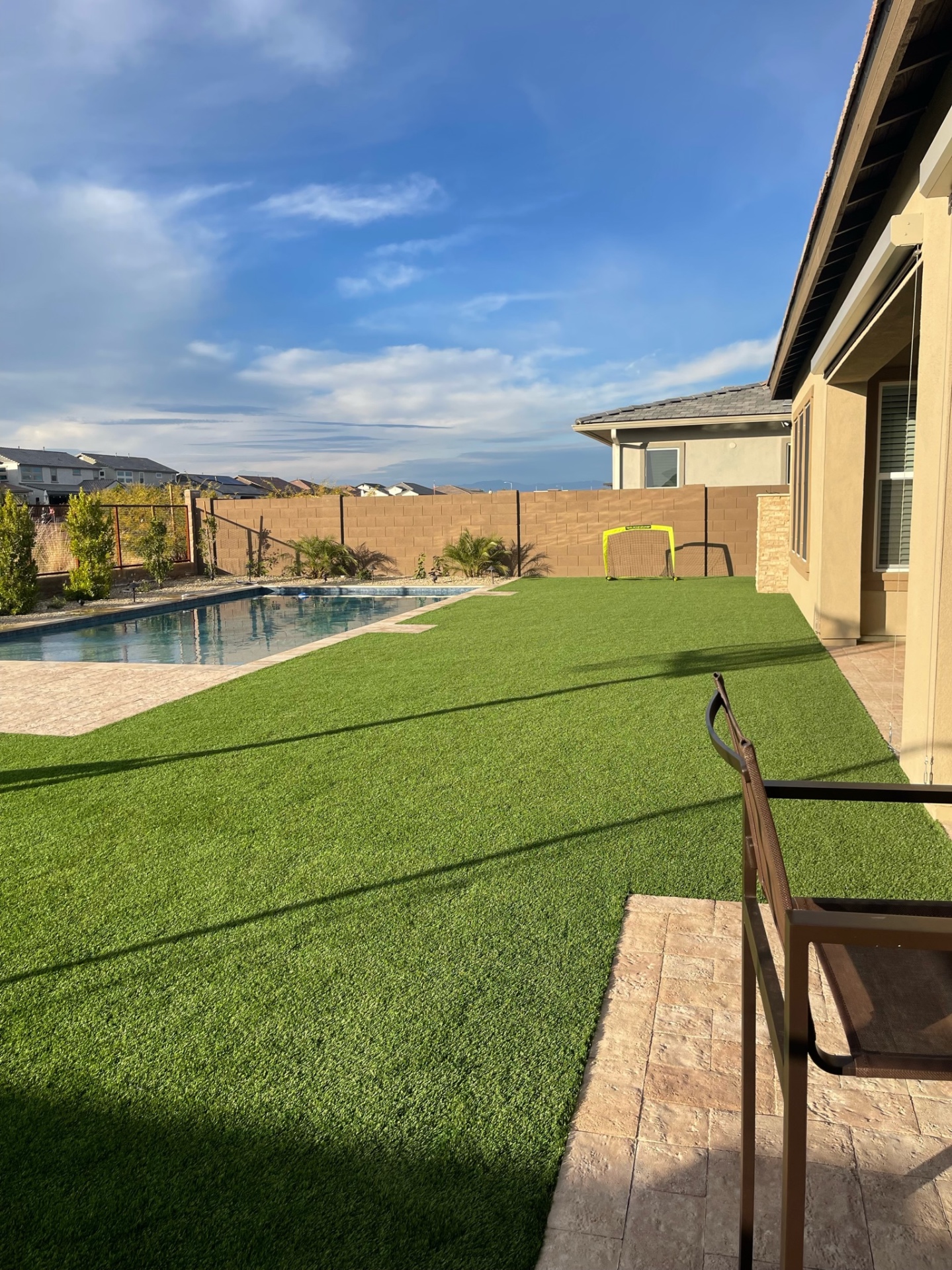 Peoria backyard artificial turf lawn tied into stamped travertine paver patio with rectangular pool and iron view fence