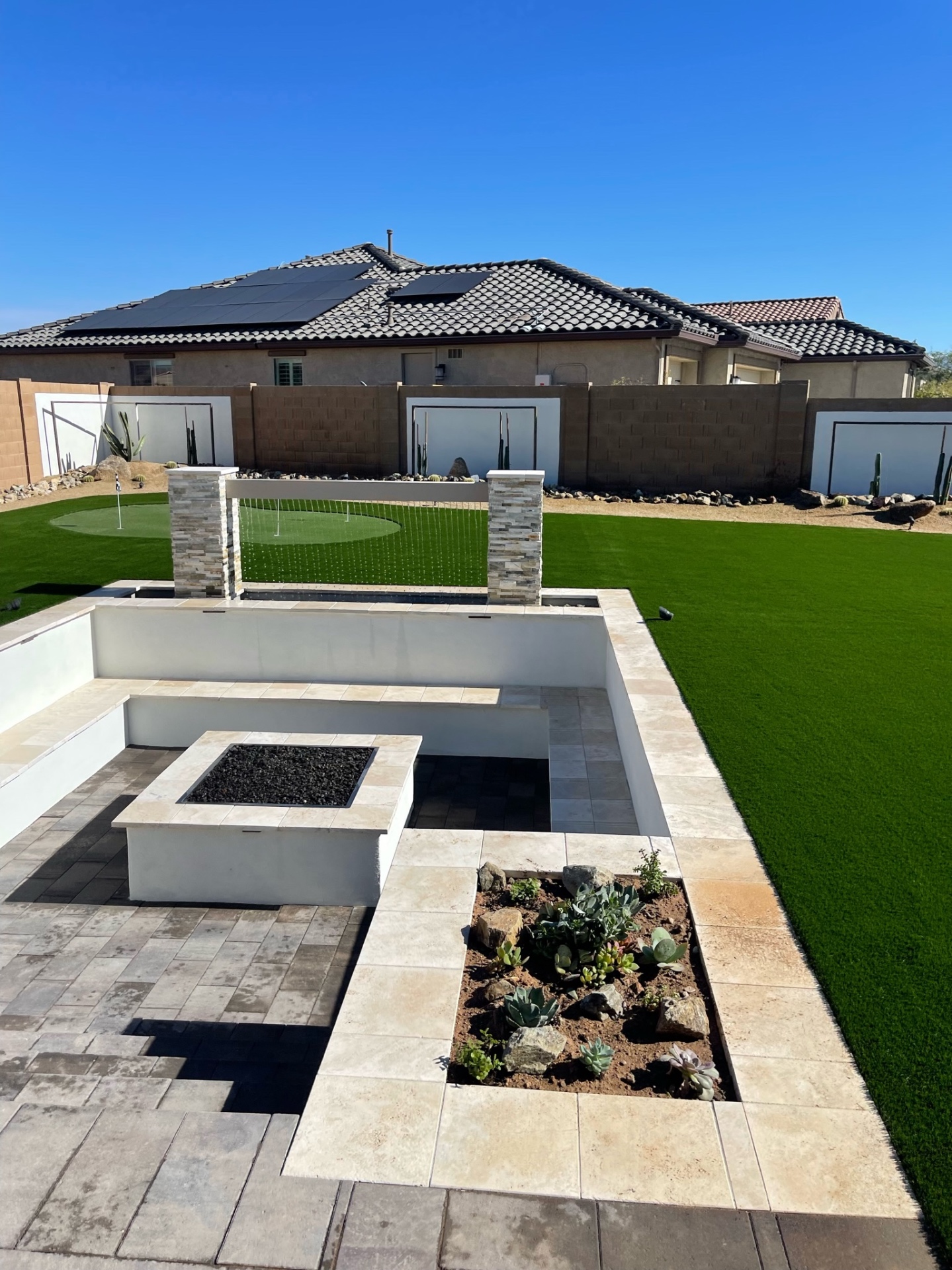 Goodyear sunken travertine firepit lounge with stacked-stone rain-curtain water feature, putting green and artificial turf lawn