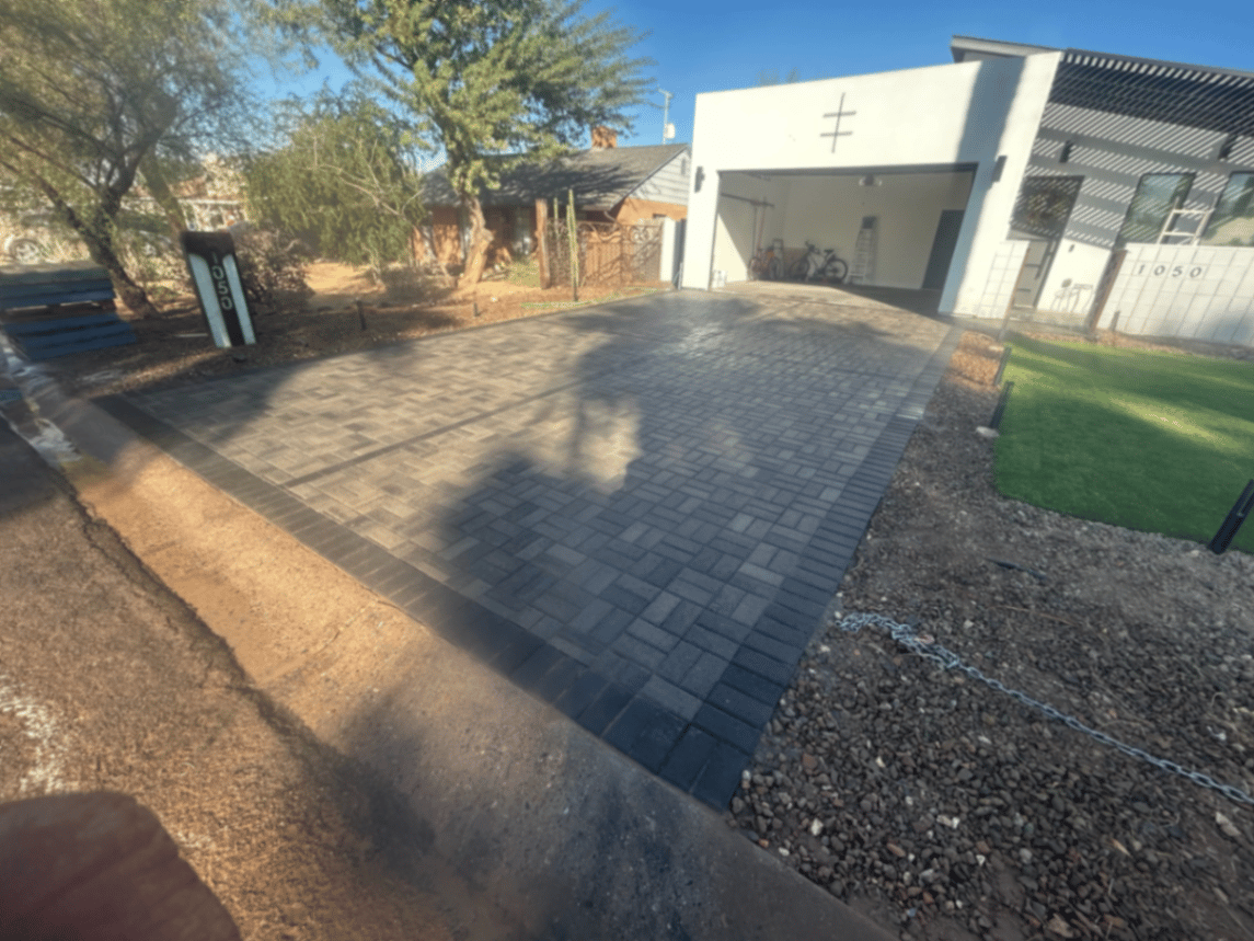 Same charcoal paver driveway seen from the street with lit address marker and turf apron.