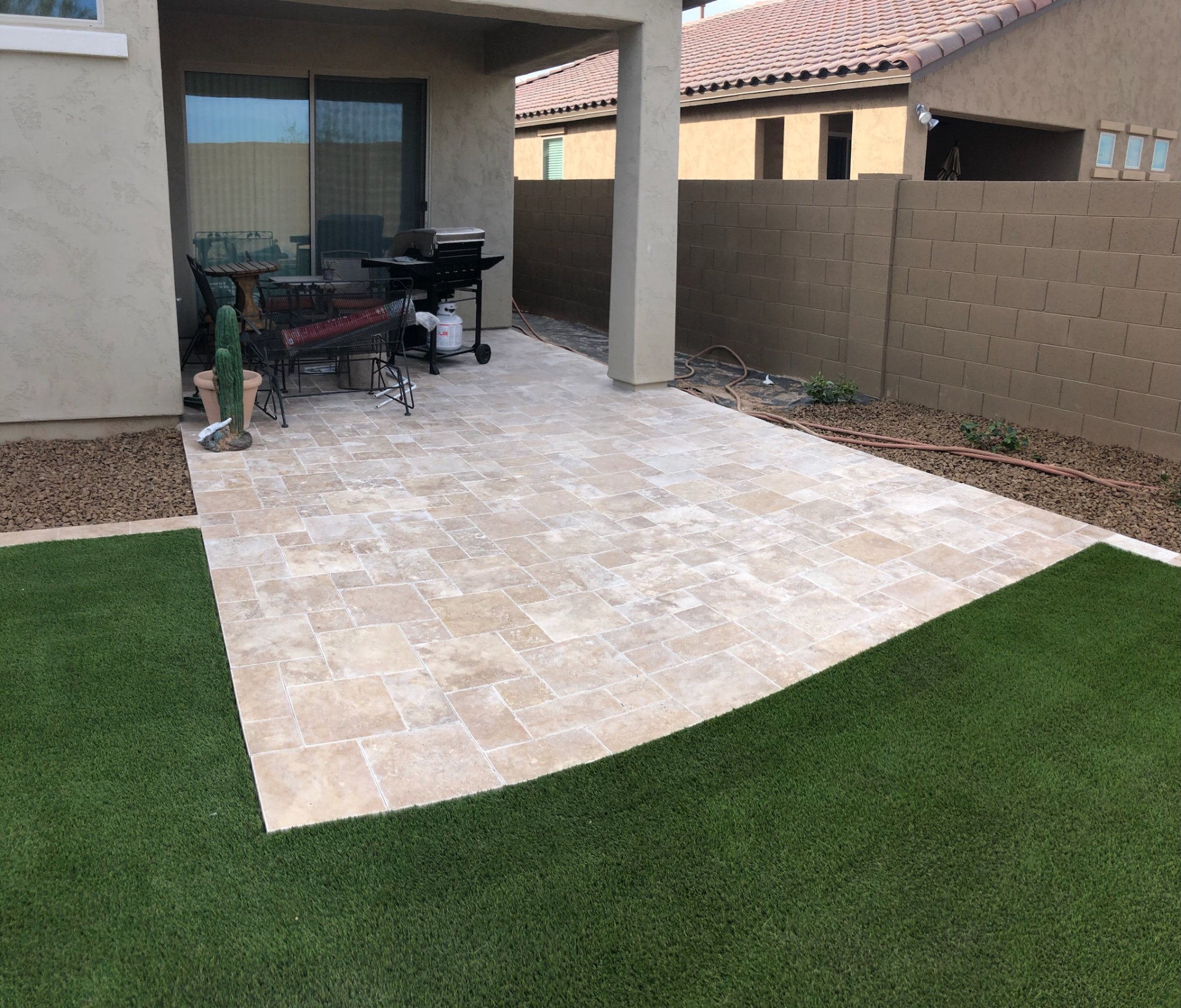 Verrado covered patio in French-pattern travertine pavers meeting a fresh artificial turf lawn