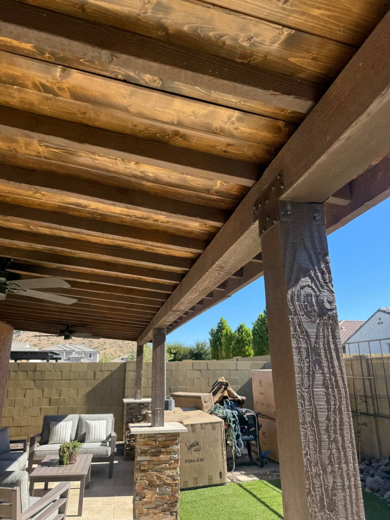 Stained wood underside of a solid-roof patio cover with exposed beam-and-rafter ceiling.