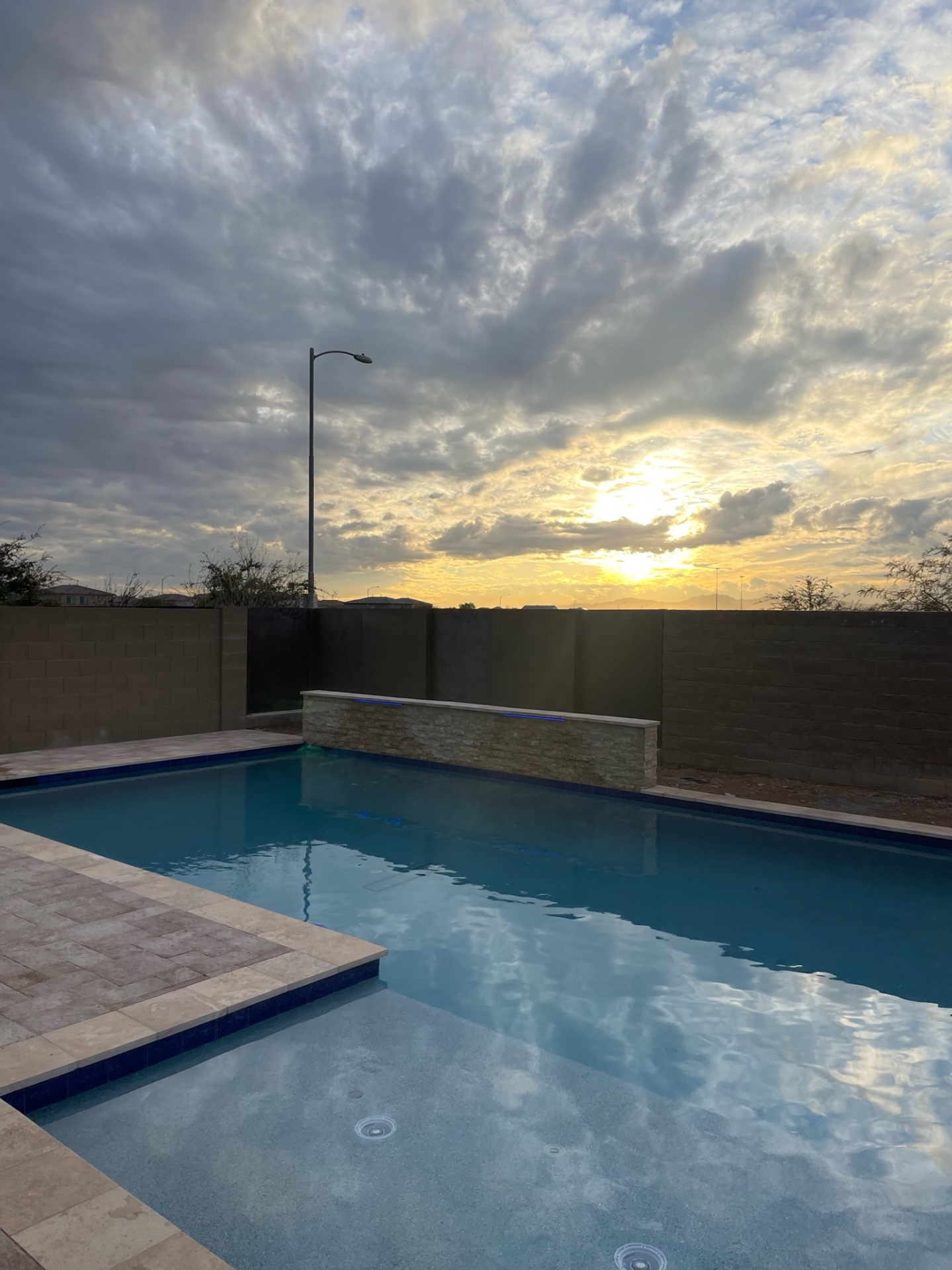 Peoria backyard geometric pool with LED-lit stacked-stone raised water feature and travertine paver deck at sunset by AE Outdoor Living